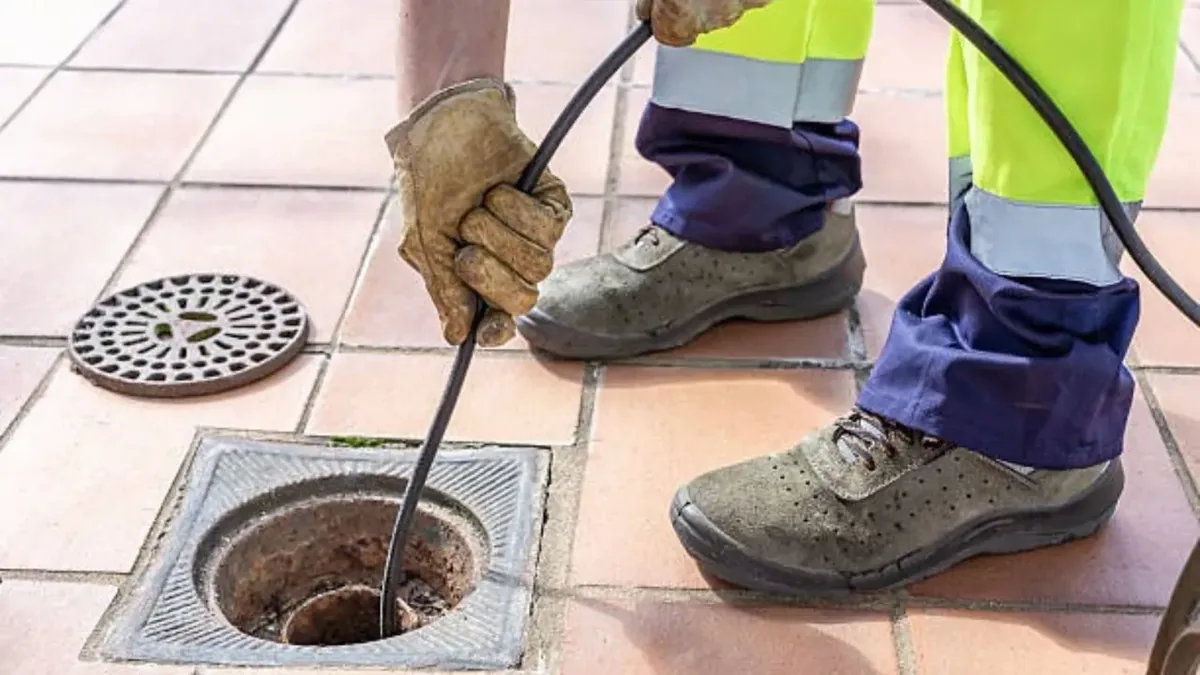 Worker feeding a cable into a tiled floor drain